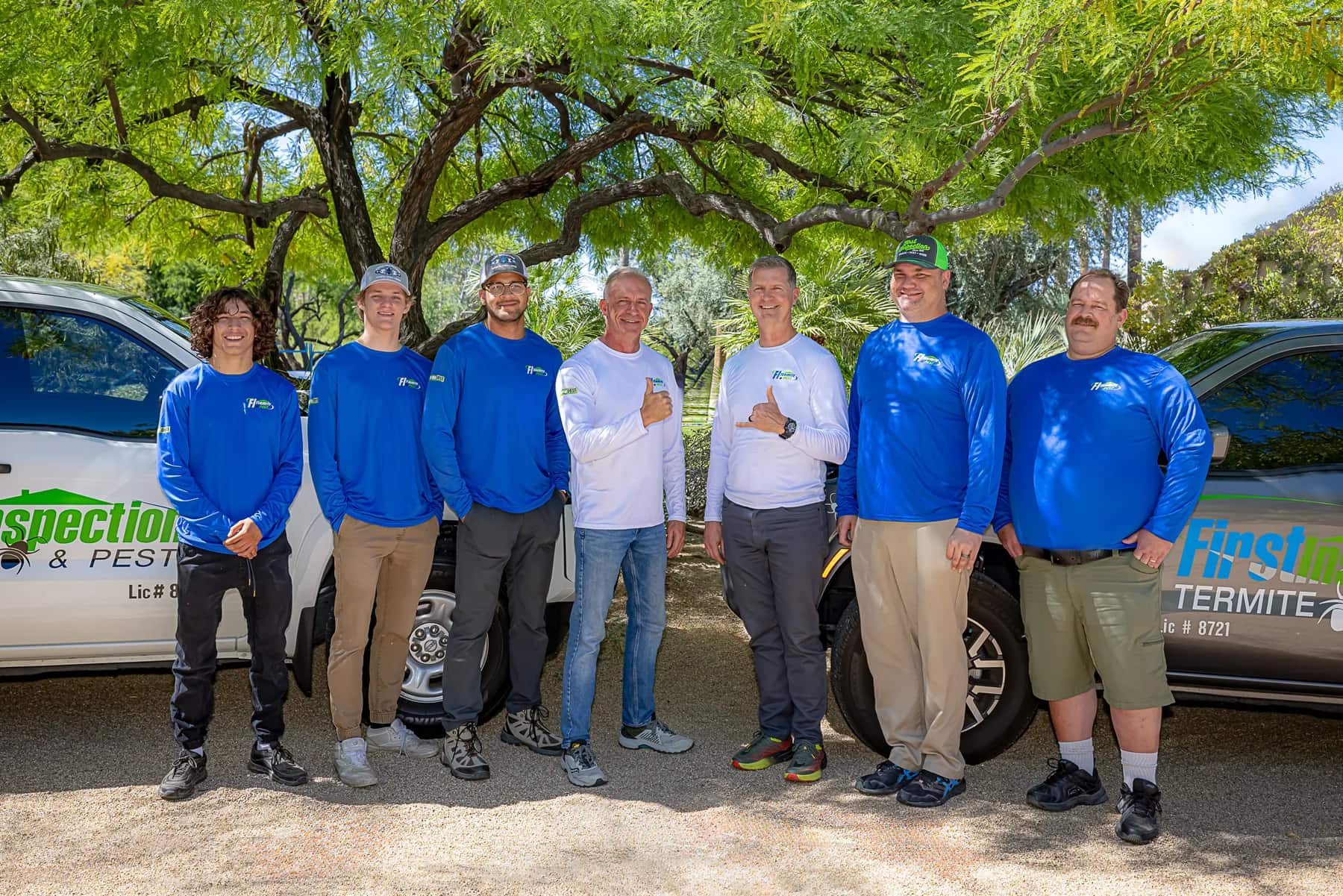 All seven members of the First Inspection Termite & Pest team standing together between two service trucks